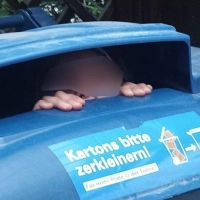 Neugierig schaut ein Kind aus einer Papiermülltonne. (Foto: -/Berufsfeuerwehr München/dpa)