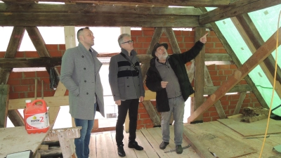 Sobald es das Wetter erlaubt, soll die Plane weg, damit das Dach eingedeckt werden kann: Architekt Hermann Keim mit Bürgermeister Patrick Ruh und KU-Vorstand Arthur Reim (von rechts) beim Baustellengespräch. (Foto: Peter Zumach)