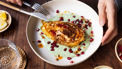 Die Spitzkohl-Viertel werden vor dem Backen kurz in der Pfanne angebraten. Nach 40 Minuten im Ofen werden sie auf Kräuterjoghurt gebettet und mit Granatapfelkernen und Walnüssen getoppt. (Foto: Zucker&Jagdwurst/zuckerjagdwurst.com/dpa-tmn)