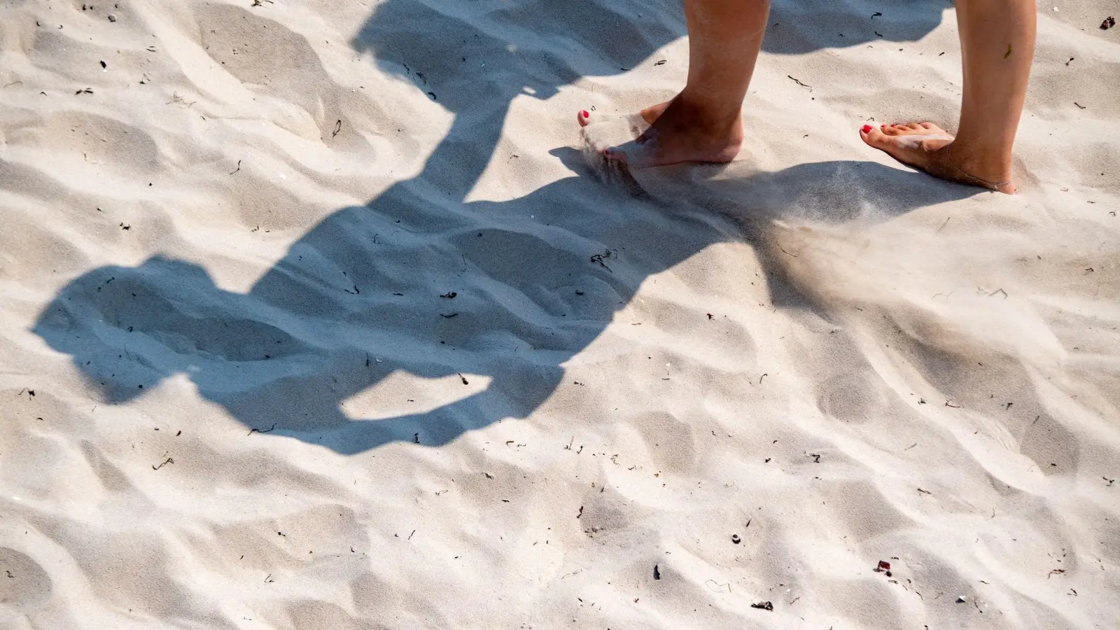 Eine Frau geht mit nackten Füßen durch den warmen Sand. (Foto: Stefan Sauer/dpa)