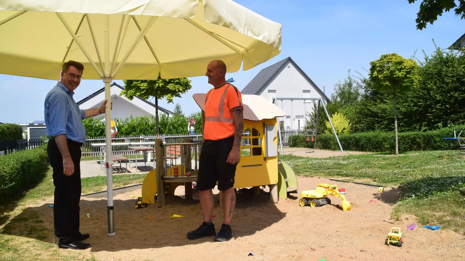 Auf dem Uffenheimer Spielplatz zwischen der Willy-Brandt-Straße und der Kurt-Schumacher-Straße steht jetzt ein Spezial-Sonnenschirm. Bürgermeister Wolfgang Lampe (links) und Bauhofleiter Thomas Siebert hoffen, damit einen Wunsch der Eltern nach mehr Schatten ein Stück weit erfüllt zu haben. (Foto: Gerhard Krämer)