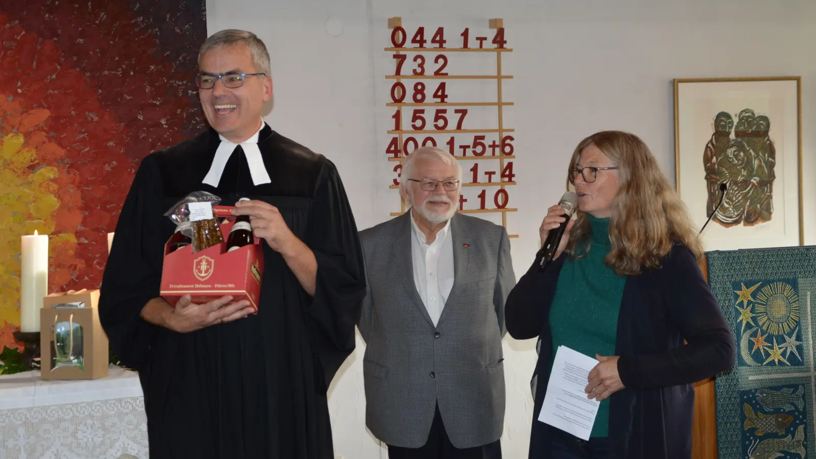 Scheinfelds scheidender evangelischer Pfarrer Joachim Roth ist in der proppenvollen Erlöserkirche mit viel Lob und Geschenken verabschiedet worden, hier etwa von Marianne Freimann von der Dekanatssynode, im Hintergrund Hans Meyer vom Kirchenvorstand. (Foto: Martina Hinkelmann)