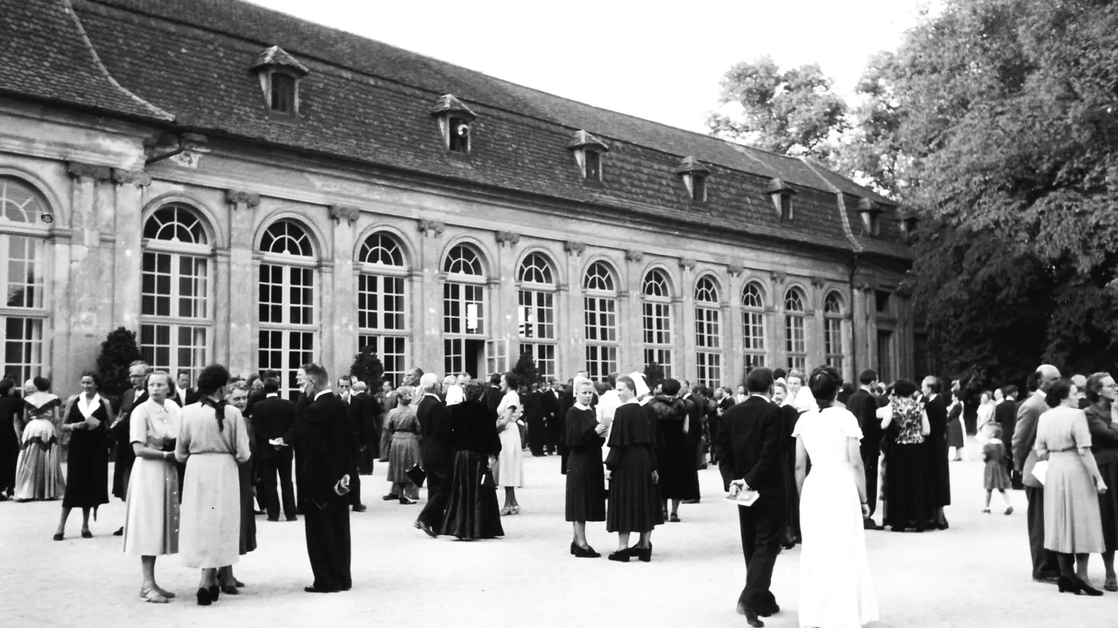 Bachwochen-Gäste flanieren in den 1950er Jahren vor der Orangerie – die Herren im dunklen Anzug, die Frauen im Kleid, lang oder wadenlang. (Foto: Bachwoche)