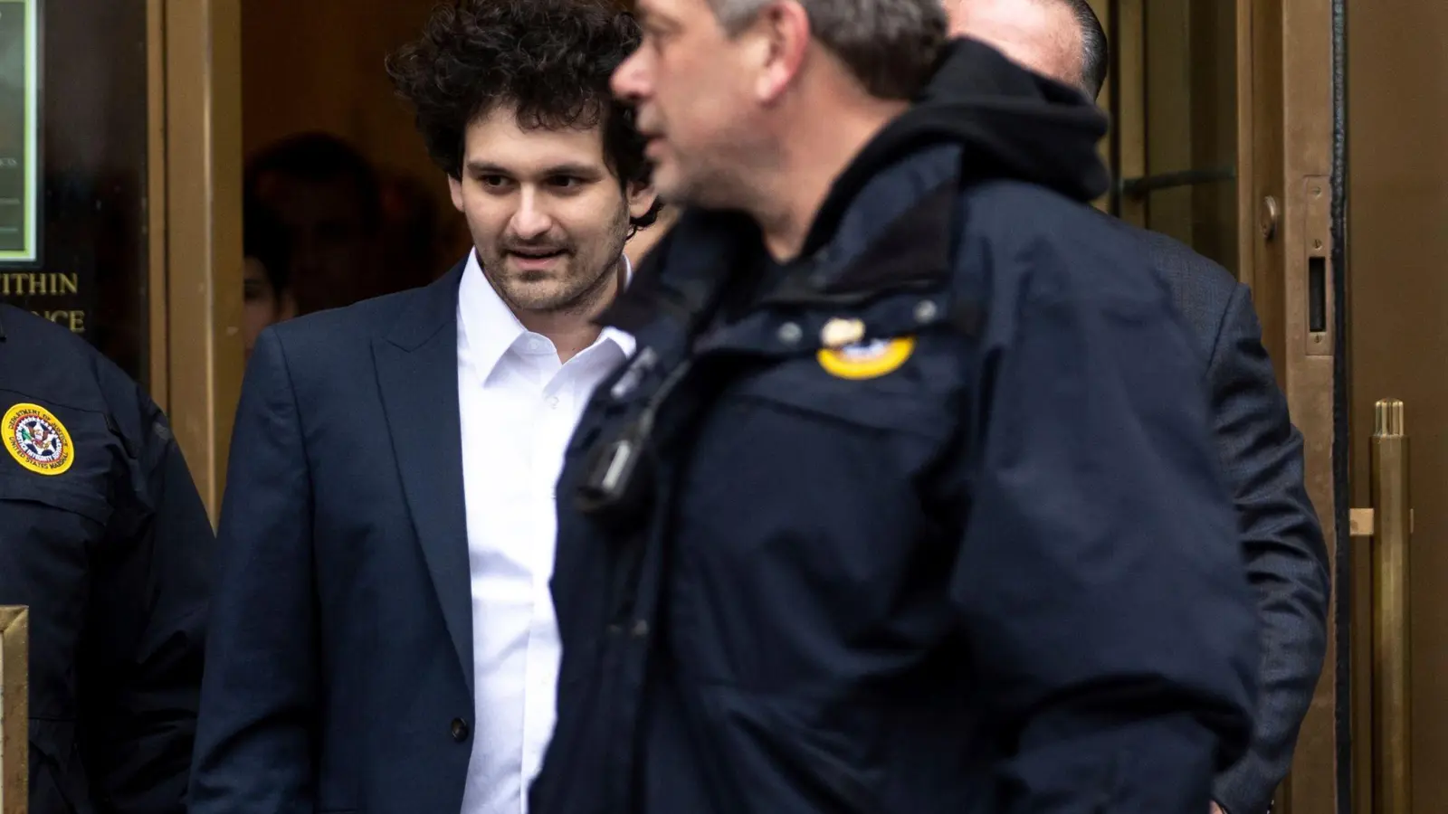 Sam Bankman-Fried (M) wird aus dem US-Bezirksgericht in Manhattan zu seinem Auto geführt. (Foto: Julia Nikhinson/AP/dpa)