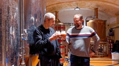 Koch Marco Gutheil-Vogt (links) und Braumeister Sebastian Meyer stoßen zwischen den Lagertanks im Herzen der kleinen Brauerei mit einer Bierprobe an. (Foto: Tizian Gerbing)