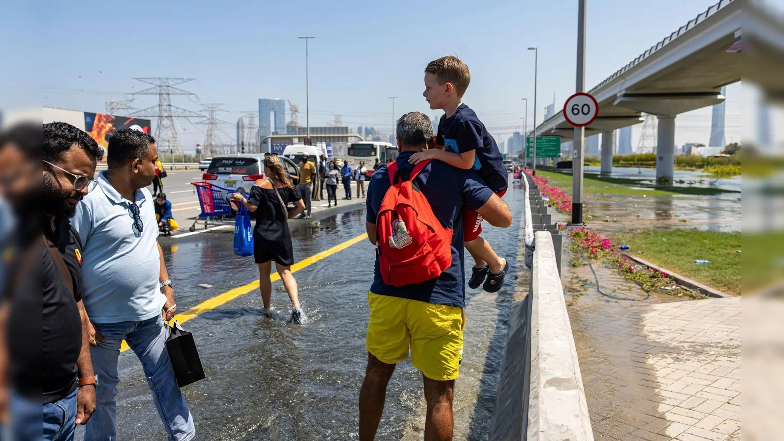 Ein Mann trägt ein Kind durch das von starkem Regen verursachte Hochwasser in Dubai. (Foto: Christopher Pike/AP/dpa)