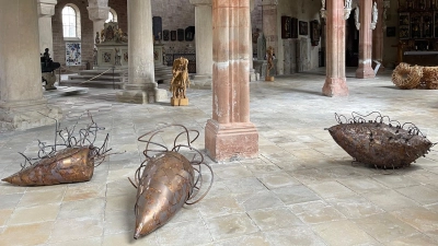 Angelika Summas Wesen aus Kupferblech und Kupferrohr erinnern an riesige Insekten, die im Mortuarium auf dem Rücken gelandet und liegengeblieben sind. Auch die Holzskulpturen im Hintergrund von Andreas Kuhnlein und Harald Kienle schaffen neue Spannungsfelder im Münster Heilsbronn. (Foto: Lara Hausleitner)