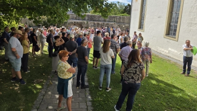 Helmut Roch (rechts) zeigte bei dem historischen Dorfspaziergang in Diespeck einer Vielzahl von Teilnehmern an der Johanneskirche interessante Details, die die Geschichte des Gebäudes erzählen können. (Foto: Rainer Weiskirchen)
