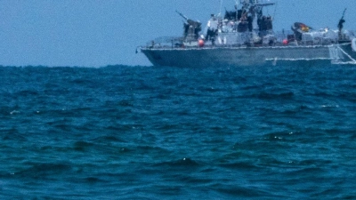 Ein Surfer wartet auf eine Welle, während ein israelisches Marineschiff im Mittelmeer vor der Küste von Hadera patrouilliert. (Foto: Ariel Schalit/AP)