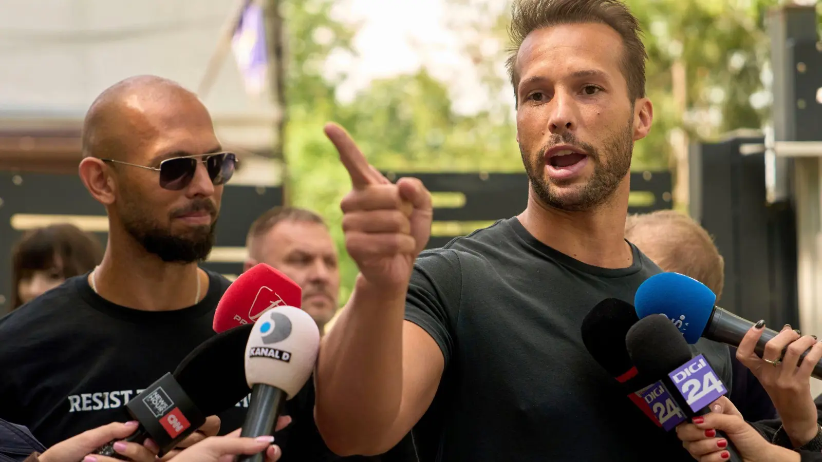 Andrew Tate (links) schaut zu seinem Bruder Tristan Tate, der am 21. Mai vor einer Polizeistation in Voluntari in Rumänien redete. (Foto: Vadim Ghirda/AP/dpa)