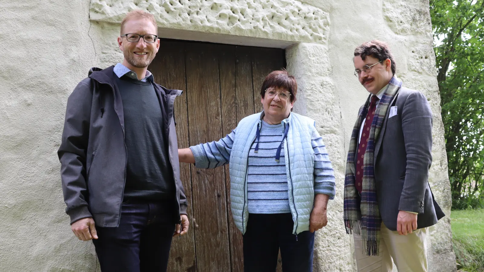 Dekan Max von Egidy, Mesnerin Angelika Arlt und Pfarrer Marvin Askani (von links) stehen vor der kleinsten Kirche im Dekanat Uffenheim, der Heilig-Kreuz-Kapelle Simmershofen. Sie ist eine von 43 Kirchengebäuden, die am Pfingstmontag von 10 bis 18 Uhr geöffnet sind.  (Foto: Claudia Pehl)