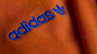 Das Logo des Sportartikelherstellers adidas in blau auf einer orangen Jacke. (Foto: Daniel Karmann/dpa)