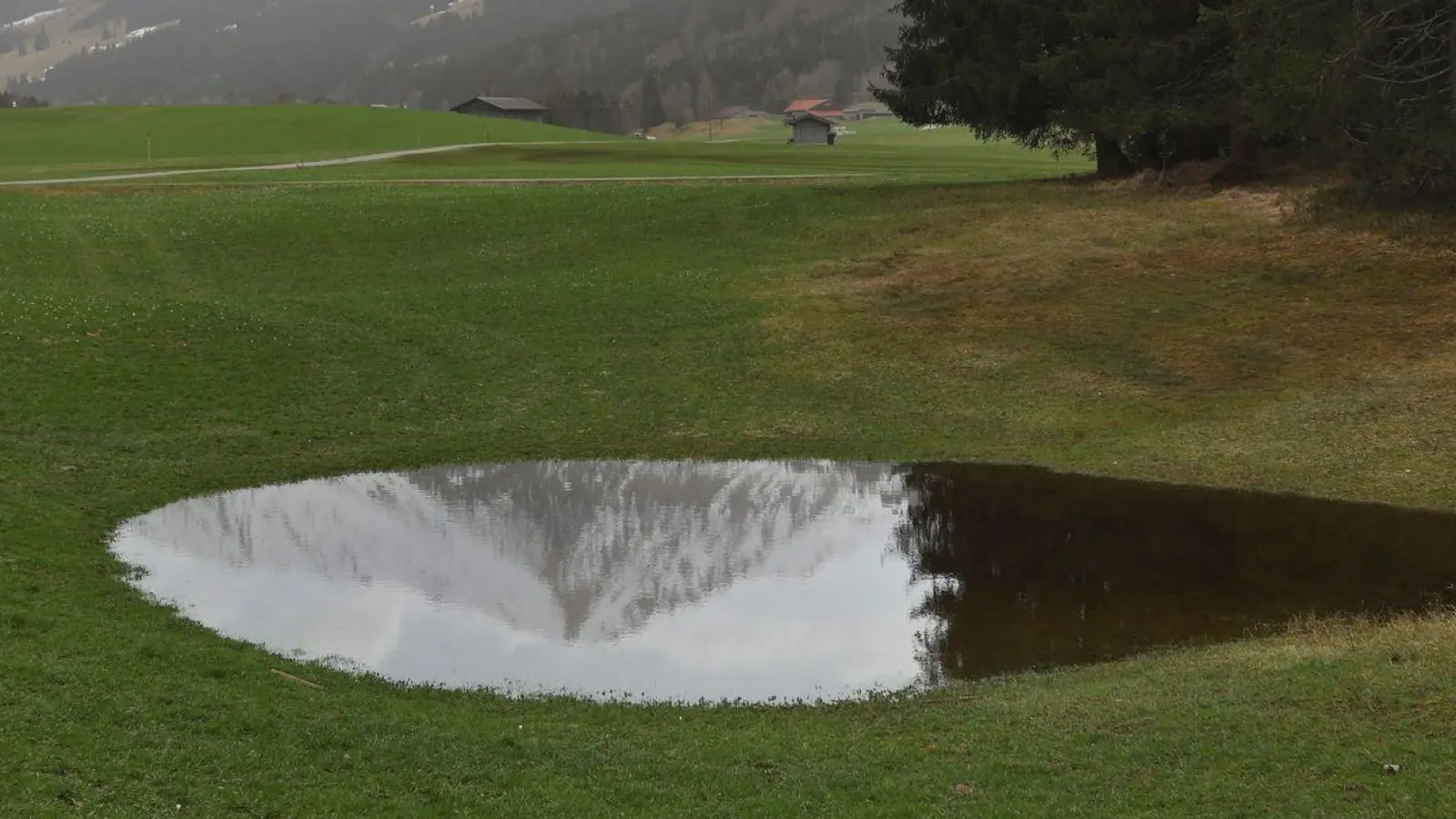 Die im Dunst liegenden Alpen spiegeln sich in einem Weiher. Der Saharastaub-Höhepunkt ist überschritten. (Foto: Karl-Josef Hildenbrand/dpa)