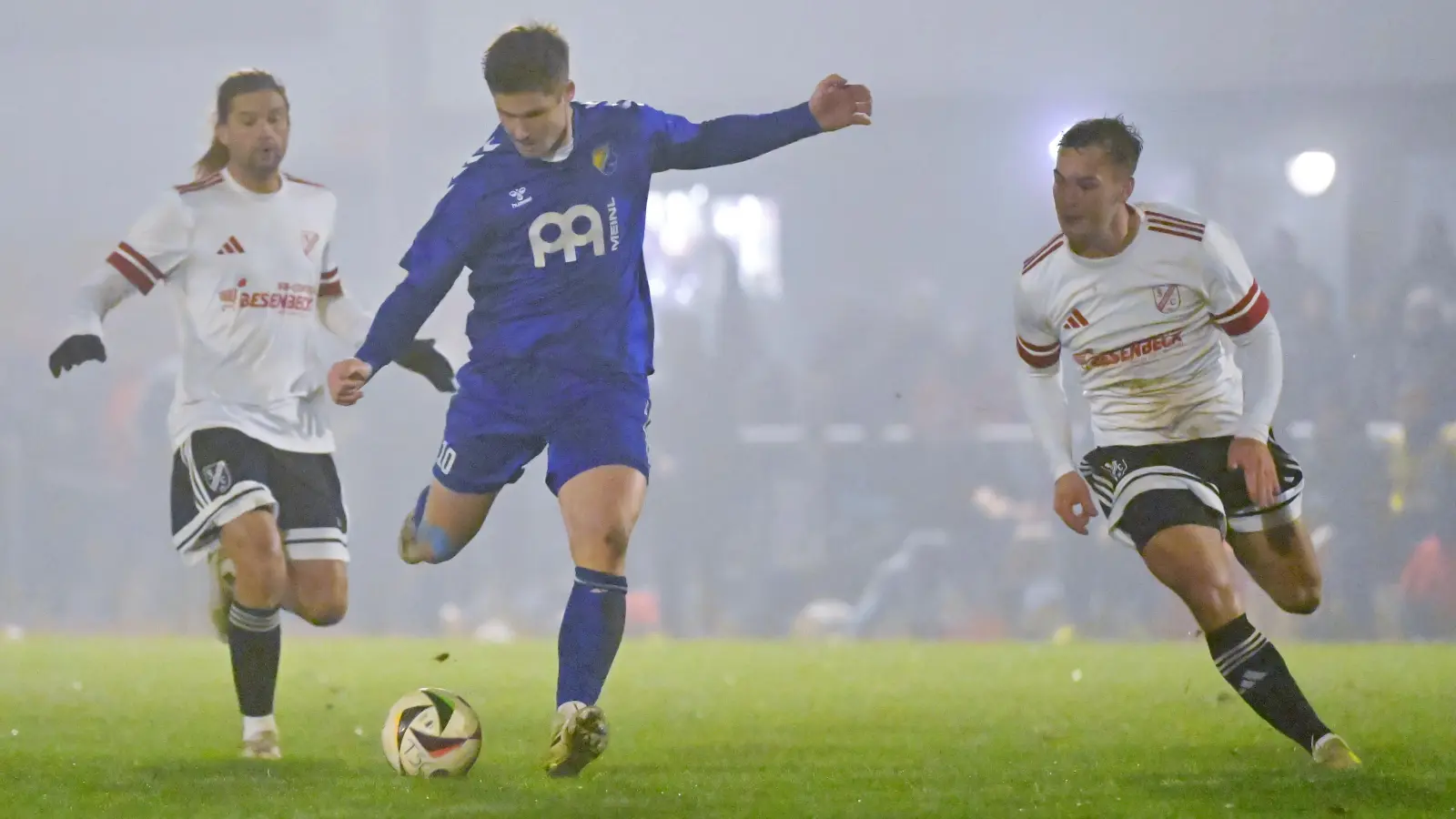 Im leichten Nebel von Neuendettelsau erzielte Dustin Lunz (in Blau) das 2:0 für Steinachgrund, hier zieht er ab und die Dettelsauer Michael Arnold (links) und Oliver Moll können es nicht verhindern. (Foto: Martin Rügner)