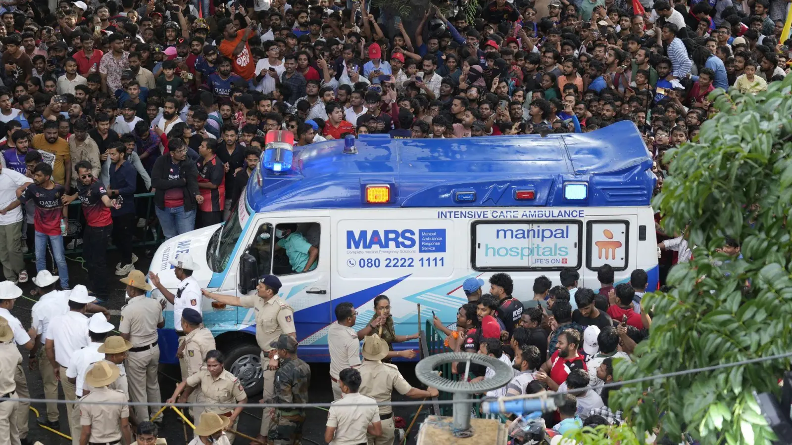 Ein Krankenwagen bahnt sich den Weg durch eine Menschenmenge am M. Chinnaswamy-Stadion in der indischen Stadt Bengaluru.  (Foto: Aijaz Rahi/AP/dpa)