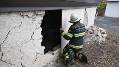 Ein Feuerwehrmann deckt das Loch in der Garagenwand ab.  (Foto: Felix Hörhager/dpa)