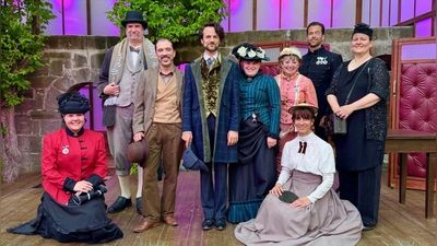 Fototermin im Sherlock-Holmes-Bühnenbild auf der Bühne im Kreuzgang: Die beiden Schauspieler Mario Schnitzler (stehend, Dritter von links) und Johann Anzenberger (stehend, Vierter von links), die Dr. John Watson und Sherlock Holmes spielen, mit Mitgliedern der Deutschen Sherlock-Holmes-Gesellschaft um deren Vorsitzende Nicole Glücklich (stehend, Vierte von rechts). (Foto: Kreuzgangspiele/ Dr. Maria Wüstenhagen)