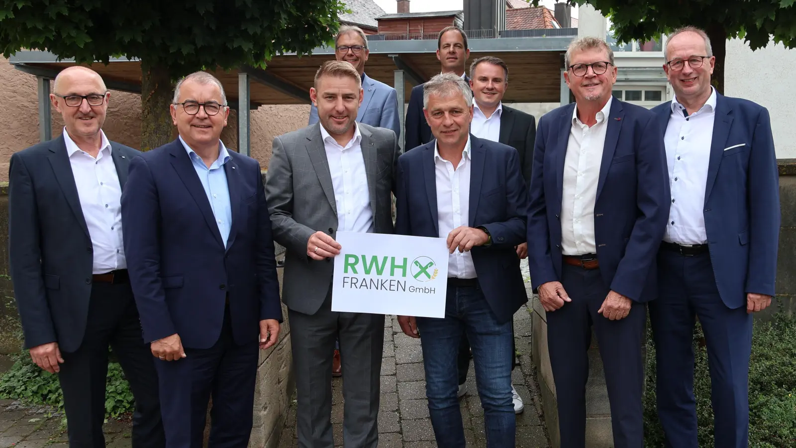 Die zwei Geschäftsführer Christian Blank und Friedrich Siemandel halten das Logo der neuen RWH Franken GmbH in die Kamera. Nicht im Foto zu sehen ist Thomas Dörr. (Foto: VR Bank im südlichen Franken eG/Petra Schörrig)