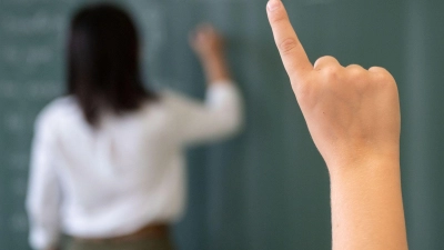 Ein Schüler meldet sich, während die Lehrerin an die Tafel schreibt. (Foto: Marijan Murat/dpa/Symbolbild)