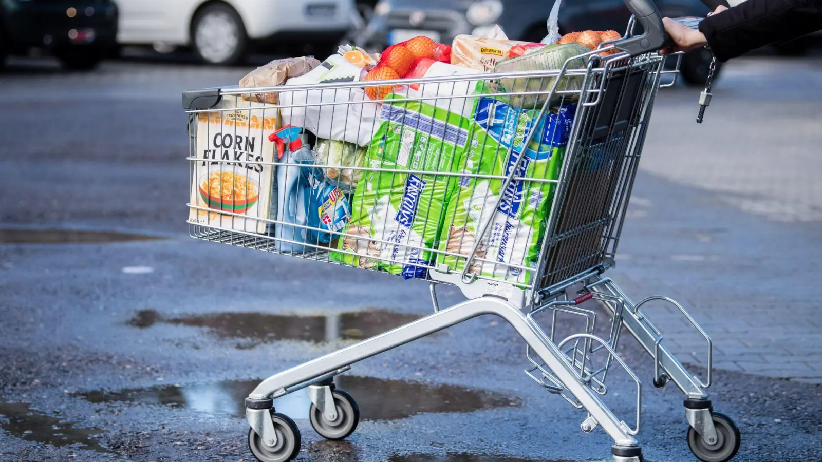 Ein Kunde schiebt einen bis zum Rand gefüllten Einkaufswagen über den Parkplatz eines Supermarktes. (Foto: Matthias Balk/dpa)