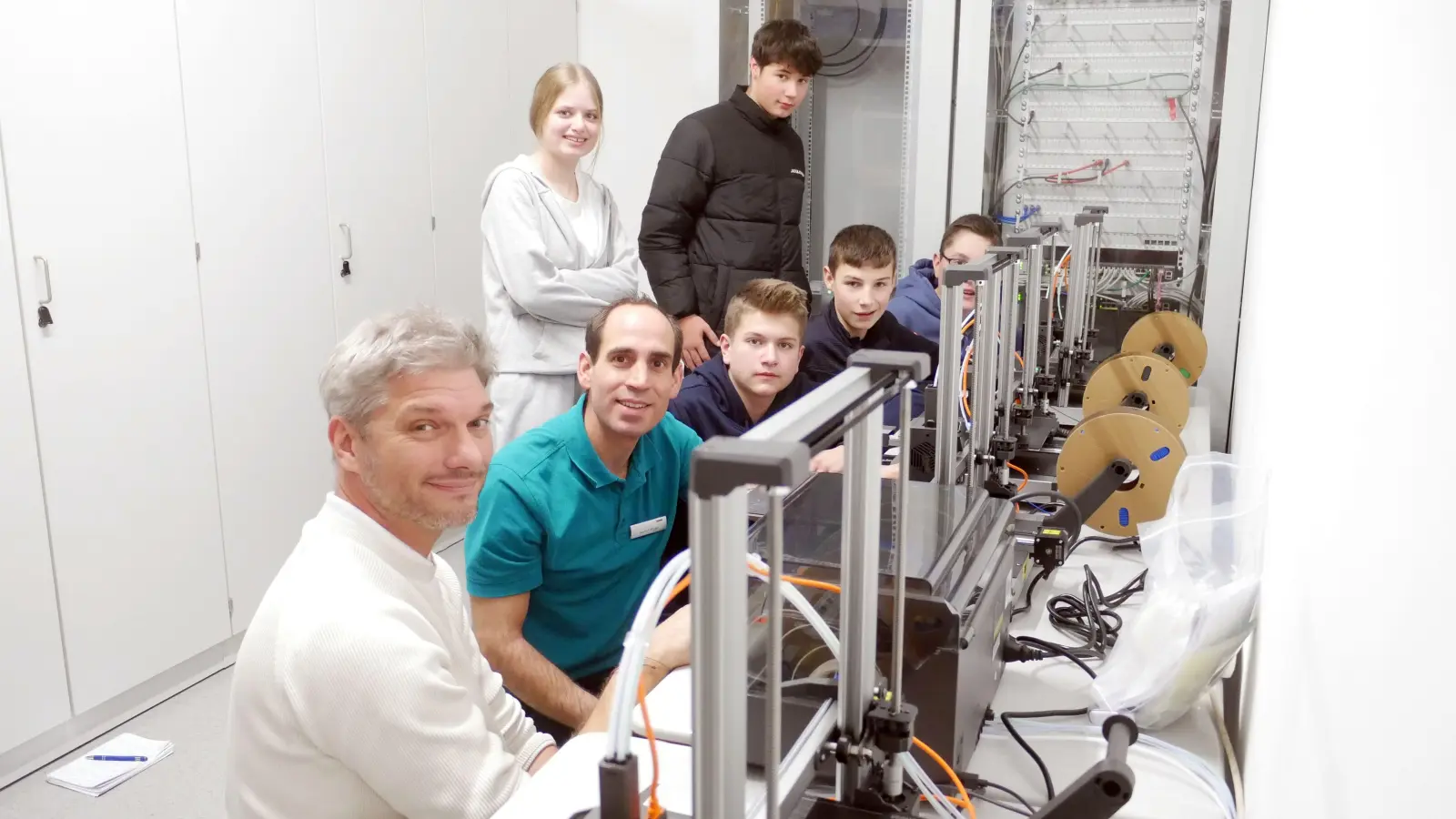 Die Schülerinnen und Schüler der Technik-Klasse sowie Mittelschulleiter Johannes Stegmann (links) ließen sich von Ausbilder Markus Mögel, der bei Rehau Automotive arbeitet, die 3D-Drucker erklären. (Foto: Lisa-Maria Liebing)