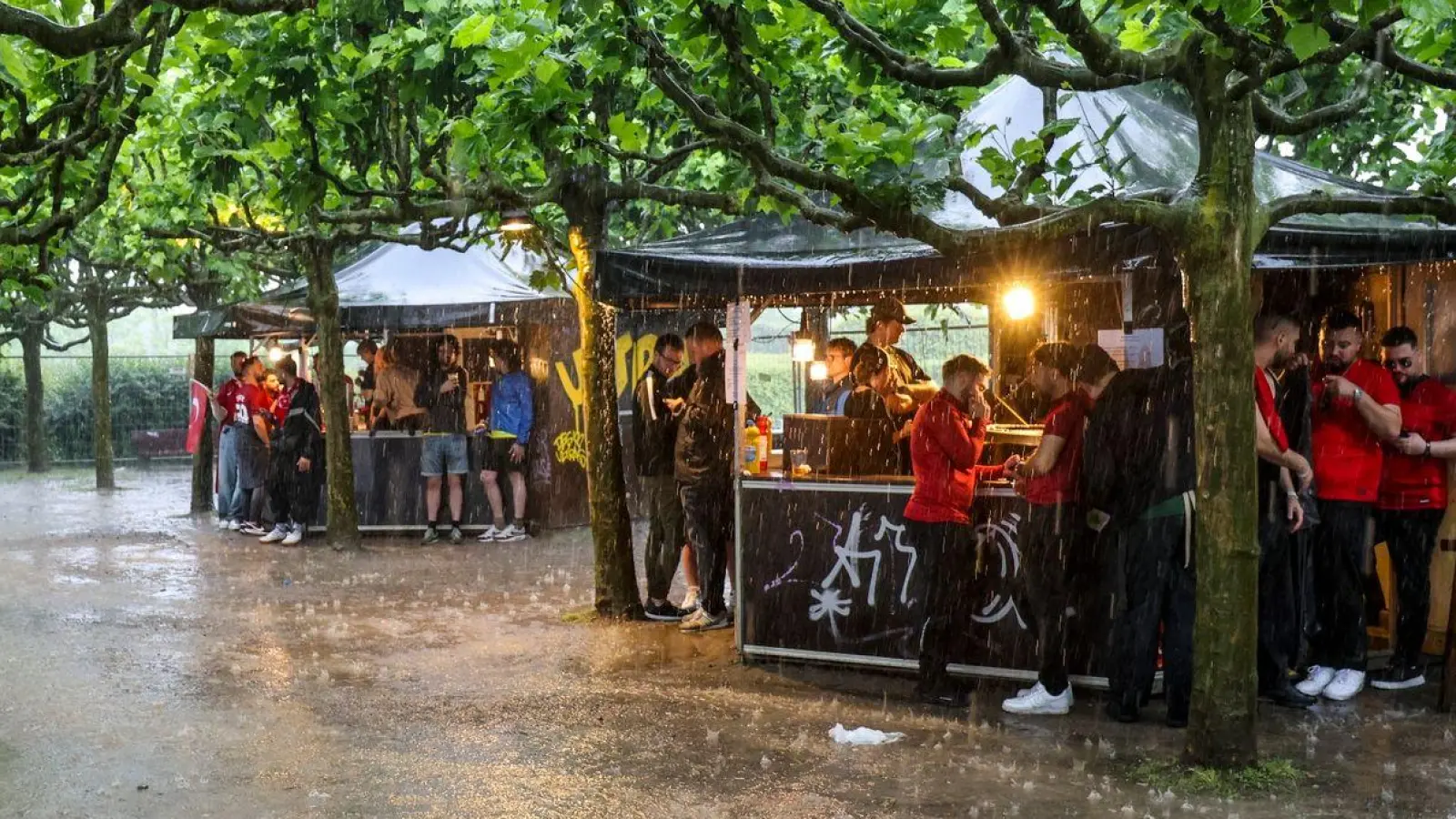 Zumindest ein bisschen Schutz: Fussballfans in Dortmund haben sich beim strömenden Regen an Imbissbuden untergestellt. (Foto: Christoph Reichwein/dpa)