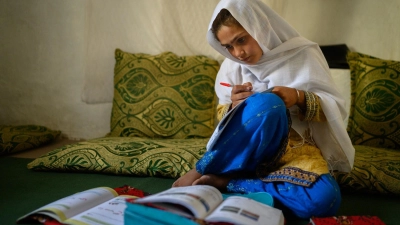 Die zehnjährige Hajira aus der afghanischen Provinz Nangarhar sitzt in einem Haus in einem abgelegenen Dorf östlich von Kabul über Schulbüchern und lernt.  (Foto: Elise Blanchard/Unicef/dpa)